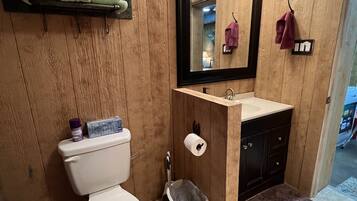 Un baño pequeño con pared de madera, inodoro blanco, lavamanos con espejo y un pequeño cubo de basura.