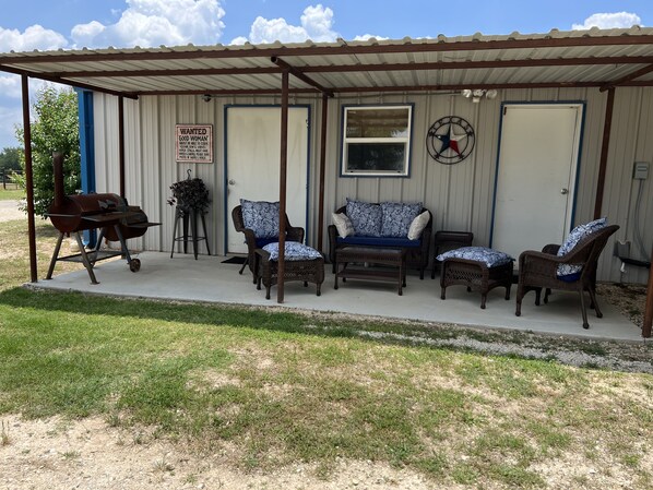 A covered outdoor seating area with wicker furniture, a barbecue grill, and a Texas flag.