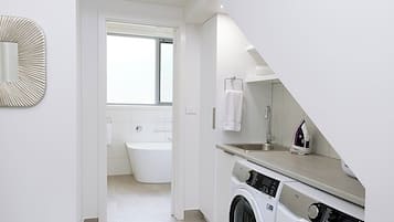 A laundry room with a washing machine and dryer, a mirror, and a view into a bathroom with a bathtub.