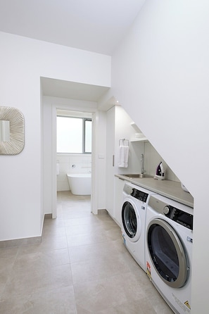 A laundry room with a washing machine and dryer, a mirror, and a view into a bathroom with a bathtub.