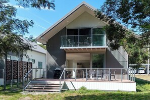 Ein modernes, zweistöckiges Haus mit einem Balkon, einer überdachten Sitzgelegenheit im Freien und einer Treppe, die zum Eingang führt.