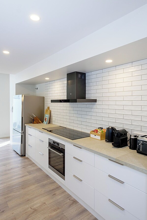 Una cocina moderna con armarios blancos, un refrigerador de acero inoxidable, un horno empotrado y una campana extractora negra.