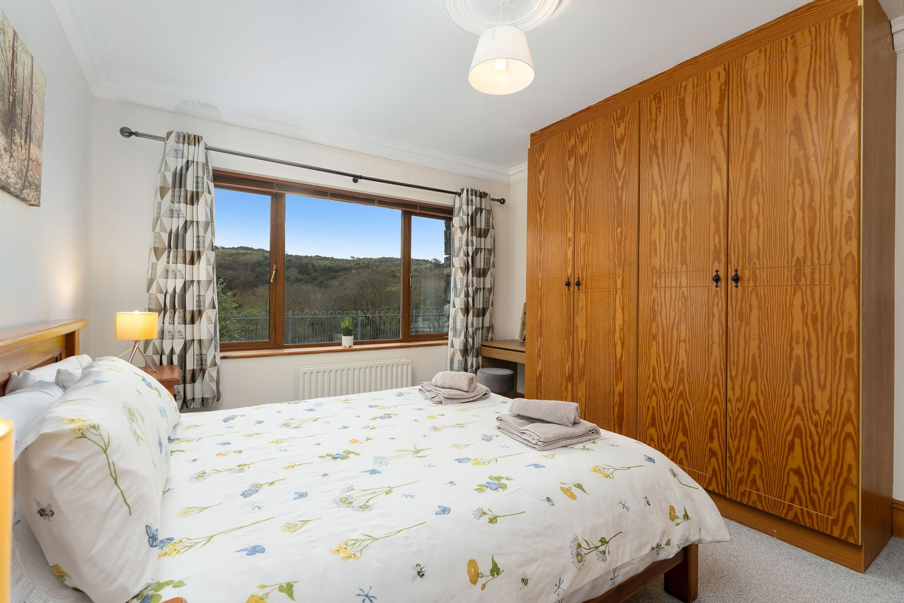Une chambre avec un grand lit, une armoire en bois, une fenêtre avec des rideaux et une vue sur l’extérieur.