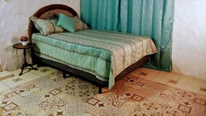 A bed with patterned bedding, a small side table with a plant, and a curtain. - Lodging near mountains (El Valle de Antón)