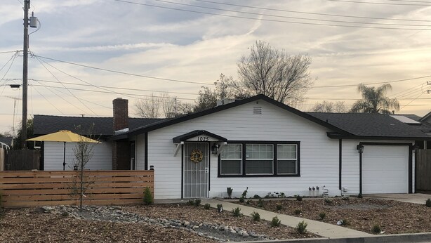A single-story house with a front porch, a small garden area with rocks and plants, and a wooden fence. - Farmhouse retreat (Tulare)