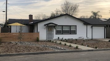 A single-story house with a front porch, a small garden area with rocks and plants, and a wooden fence.