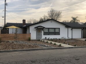 A single-story house with a front porch, a small garden area with rocks and plants, and a wooden fence. - Farmhouse retreat (Tulare)