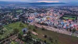 An aerial view of a city with a mix of residential and commercial buildings, a large open area, and a body of water in the distance.
