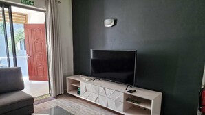 A modern living room with a flat-screen TV on a white entertainment unit, a dark-colored sofa, and a glass coffee table. - Sugareef 3-Bed Apartment in Flic en Flac (Flic en Flac)