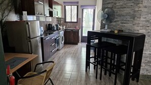 A modern kitchen with dark wooden cabinets, stainless steel appliances, a dining area with a table and chairs, and a large window with a view of greenery. - Sugareef 3-Bed Apartment in Flic en Flac (Flic en Flac)
