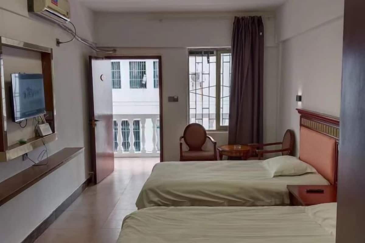 A hotel room with two beds, a TV, a chair, a small table, and a balcony with a view.