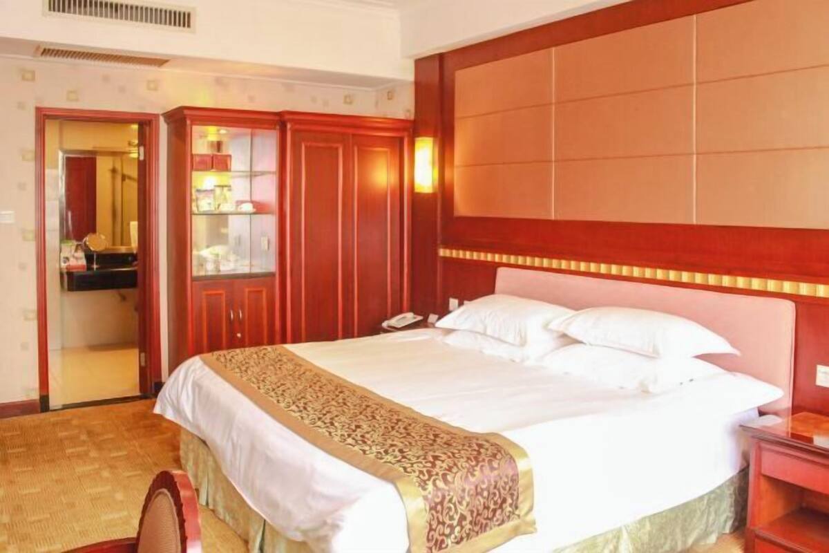 A hotel room with a large bed, a wooden wardrobe, a bedside table, and a mirror.