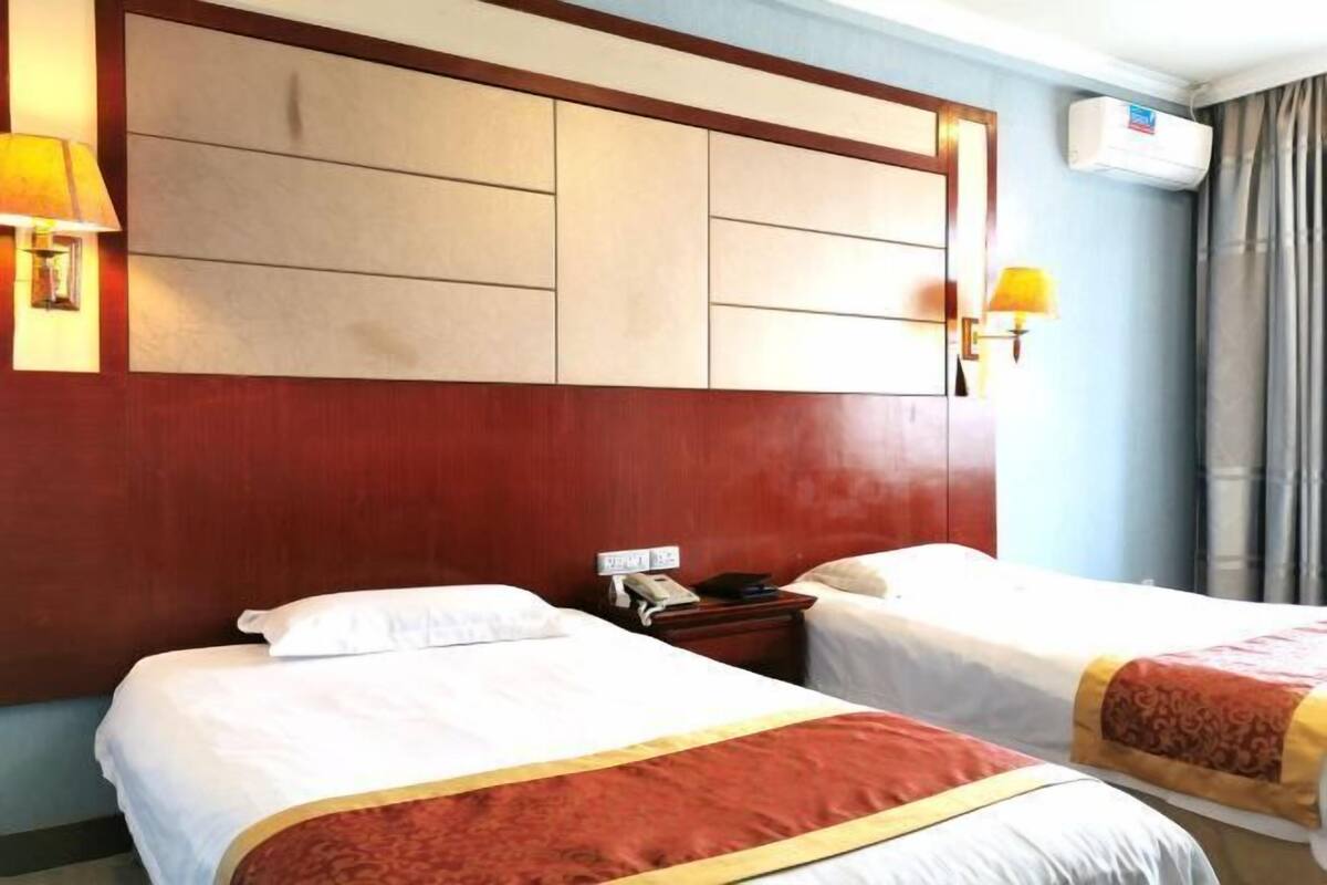 A hotel room with two beds, a wooden headboard, a telephone, and a wall-mounted air conditioner.