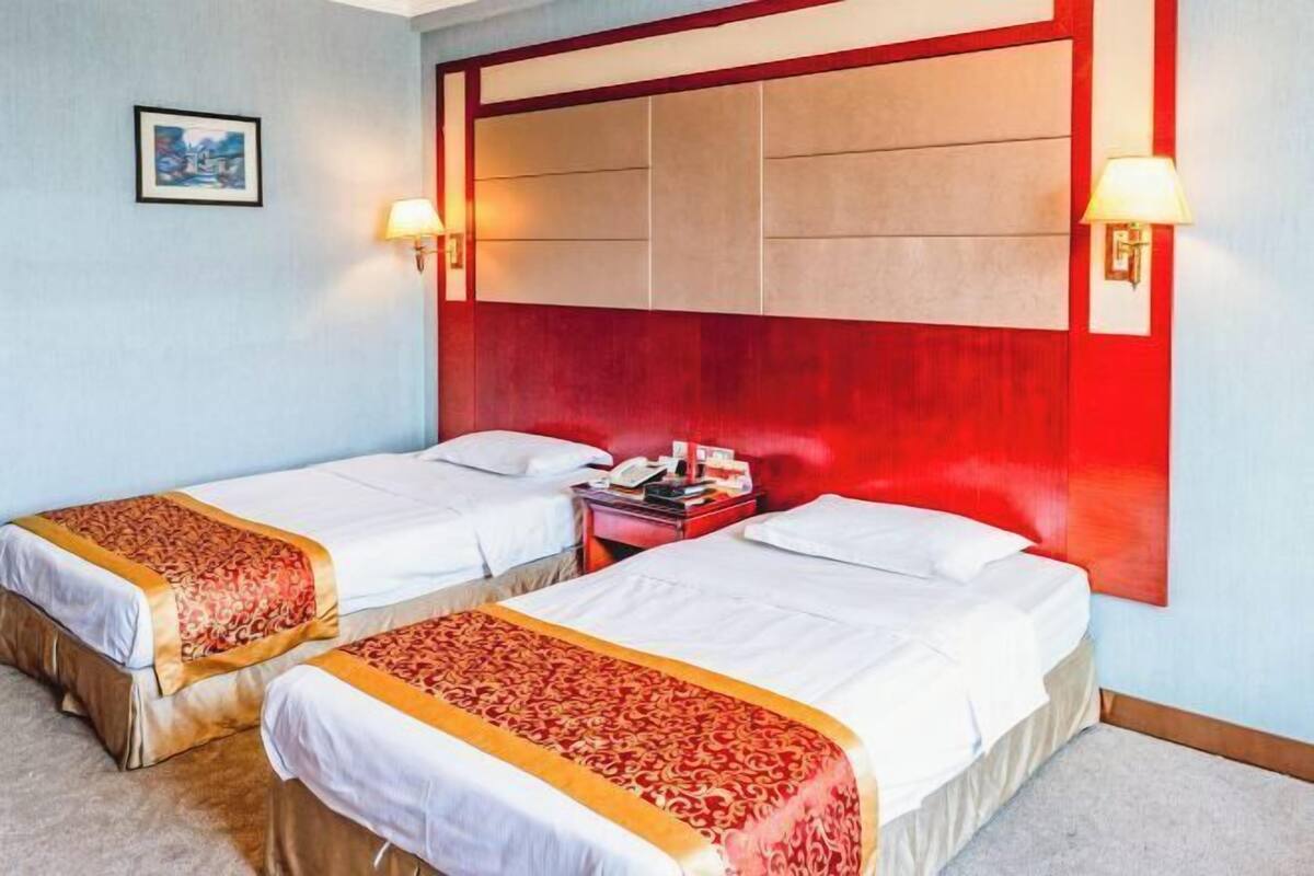 A hotel room with two beds, a red headboard, bedside lamps, and a framed picture on the wall.