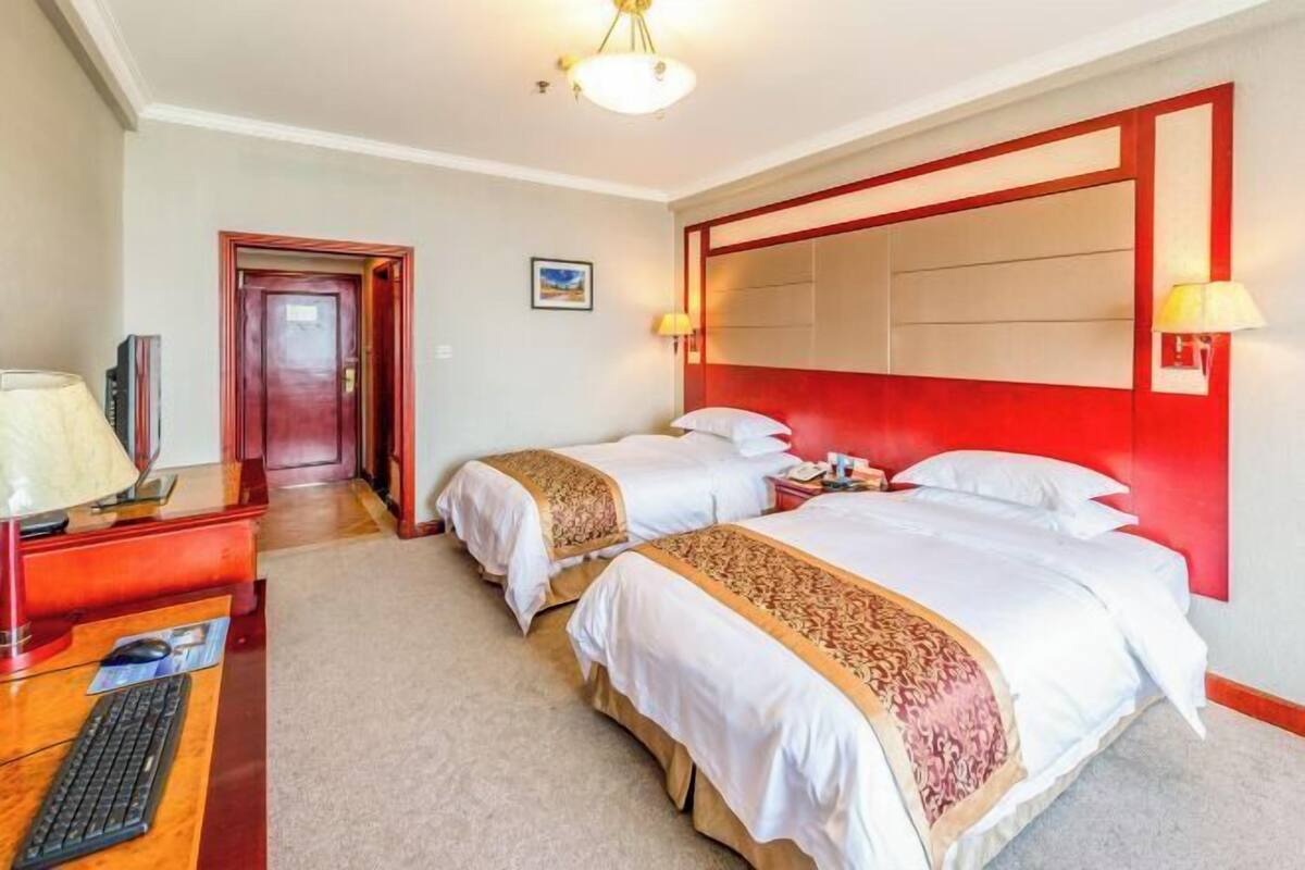 A hotel room with two beds, a desk with a computer, and a red accent wall.