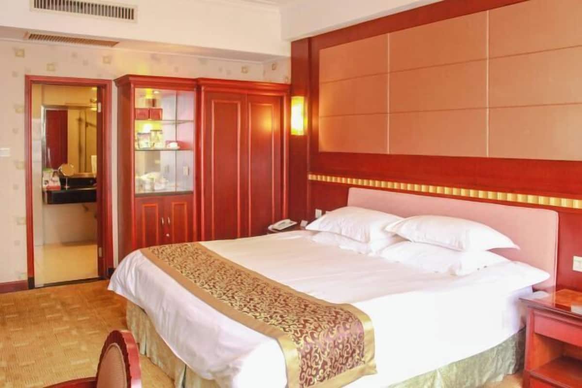 A hotel room with a large bed, a wooden wardrobe, and a mirror.
