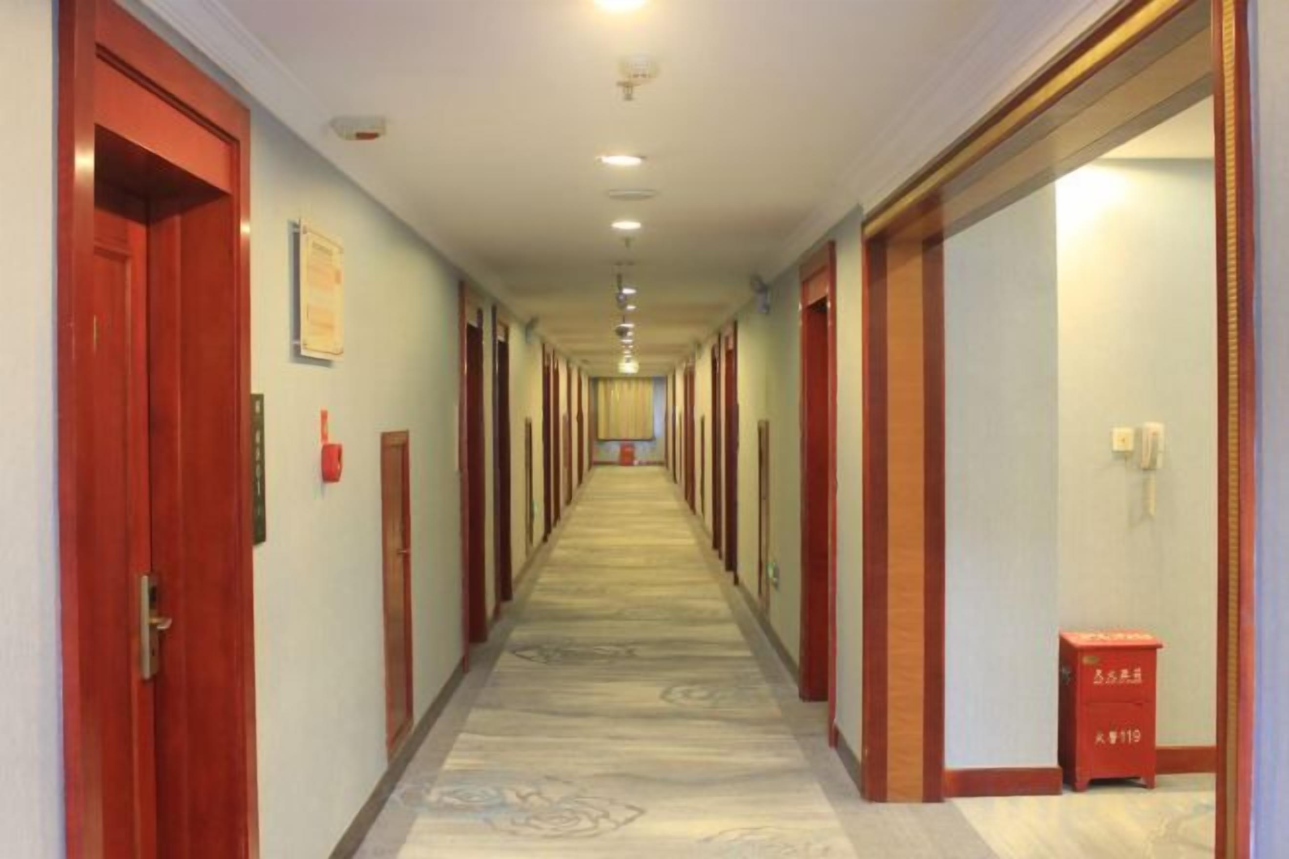 Pasillo de hotel con puertas a ambos lados, alfombra estampada y un cesto de basura.