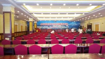 Un salón de conferencias con filas de mesas y sillas, un escenario con un banner y un mural grande en la pared.