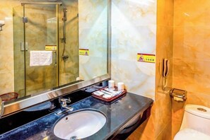 Un baño con pared de mármol, cabina de ducha de vidrio, lavabo con artículos de aseo e inodoro.