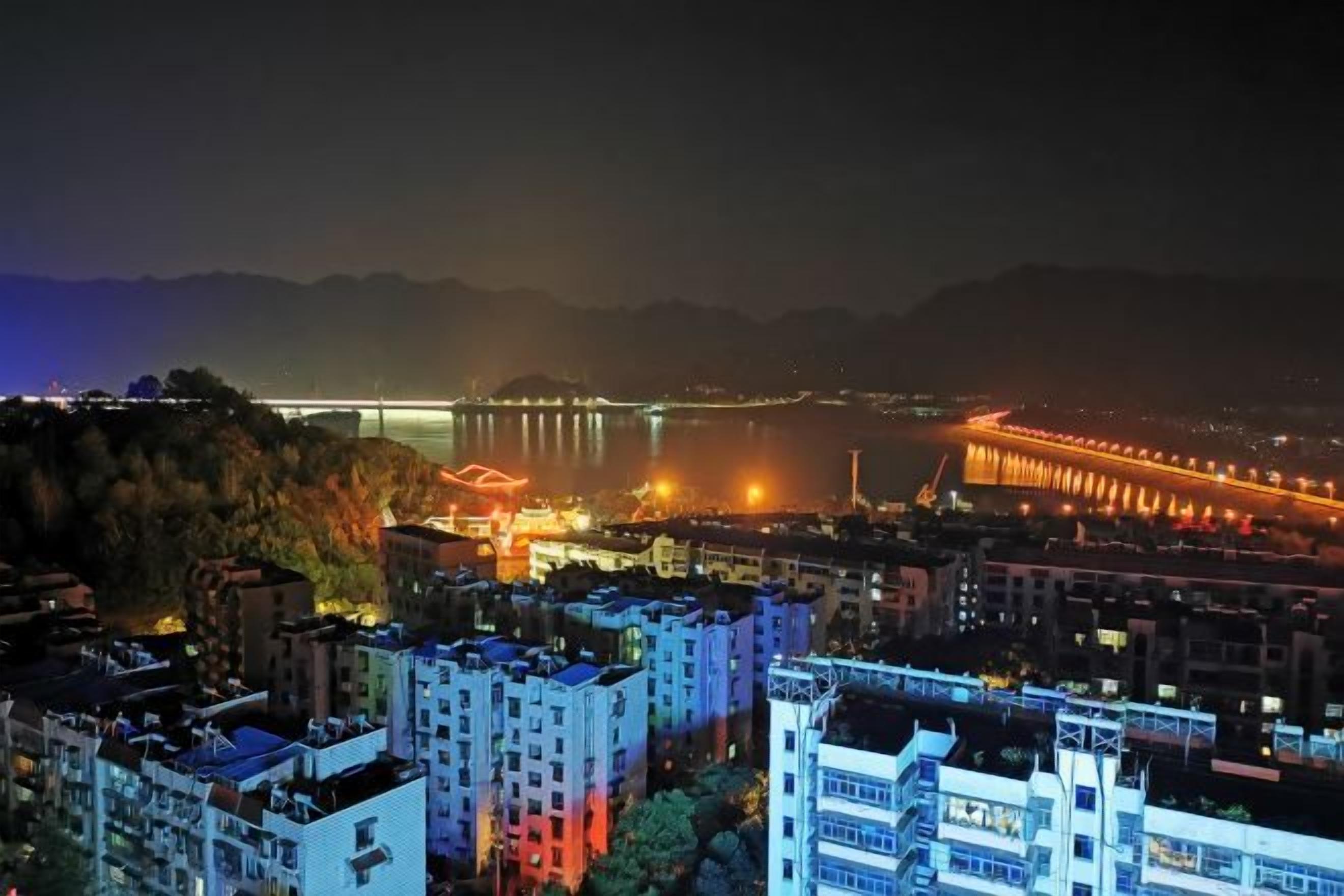 A nighttime cityscape with illuminated buildings and a bridge in the distance.