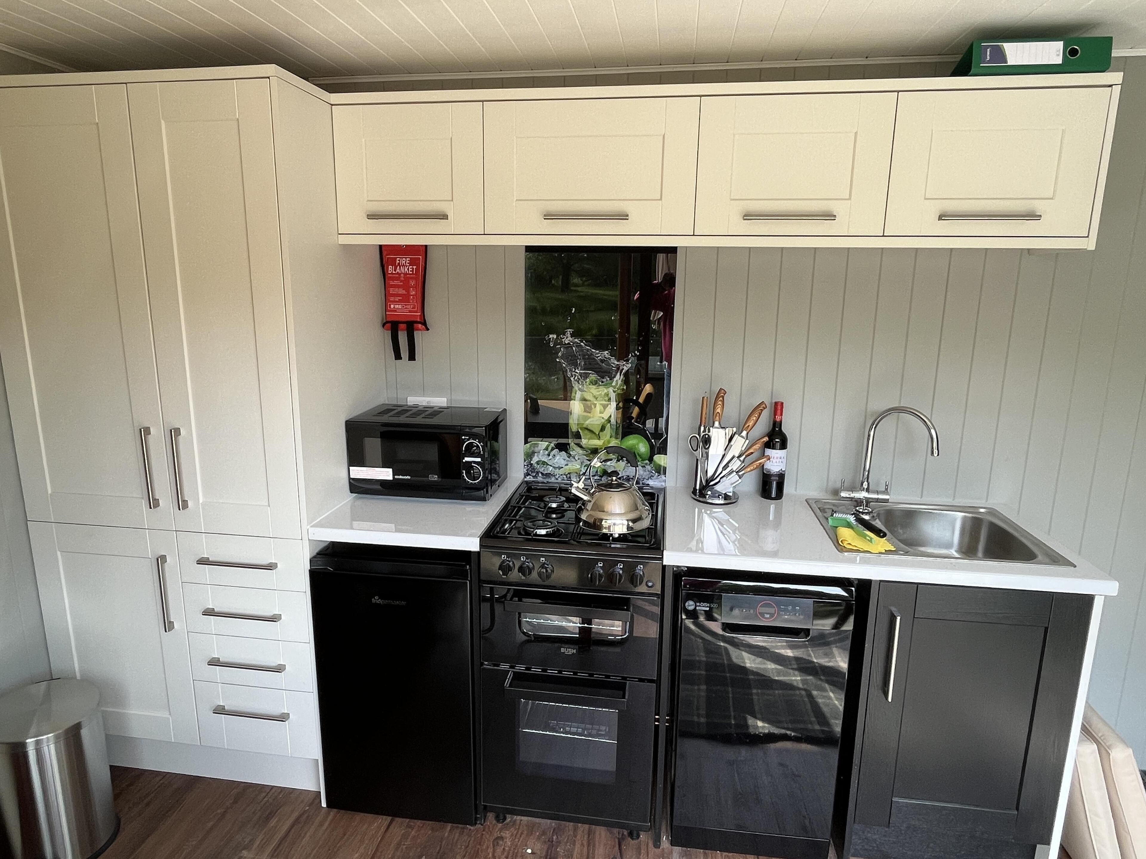 A compact kitchen with white cabinets, a black microwave, a stove, an oven, and a dishwasher.