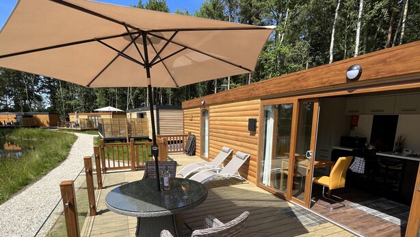 Een houten terras met een glazen deur naar een keuken, een ronde tafel met stoelen en een grote parasol.