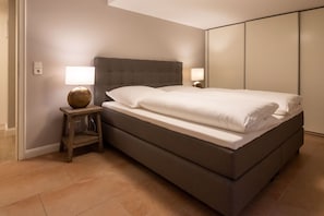 A modern bedroom with a large bed, a nightstand with a lamp, and a wardrobe. - Achter Dünem, Whg. 4 - Strandnahe 3-zimmer Ferienwohnung auf 70 m² Wohnfläche, für bis zu 4 Personen (Wenningstedt-Braderup (Sylt))