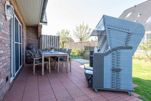 Une terrasse extérieure avec une table et des chaises en bois, un barbecue et un mur en briques.