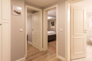 A hallway with a bed in the background, a bathroom with a marble sink, and a door leading to another room.