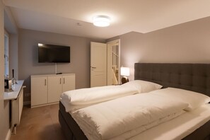 Ein Hotelzimmer mit zwei Betten, einem an der Wand befestigten Fernseher, einem Schreibtisch mit Lampe und einem Kleiderschrank.