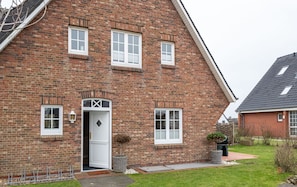 A brick house with a white door, multiple windows, and a small garden.
