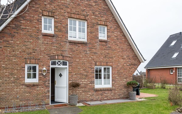 A brick house with a white door, multiple windows, and a small garden.