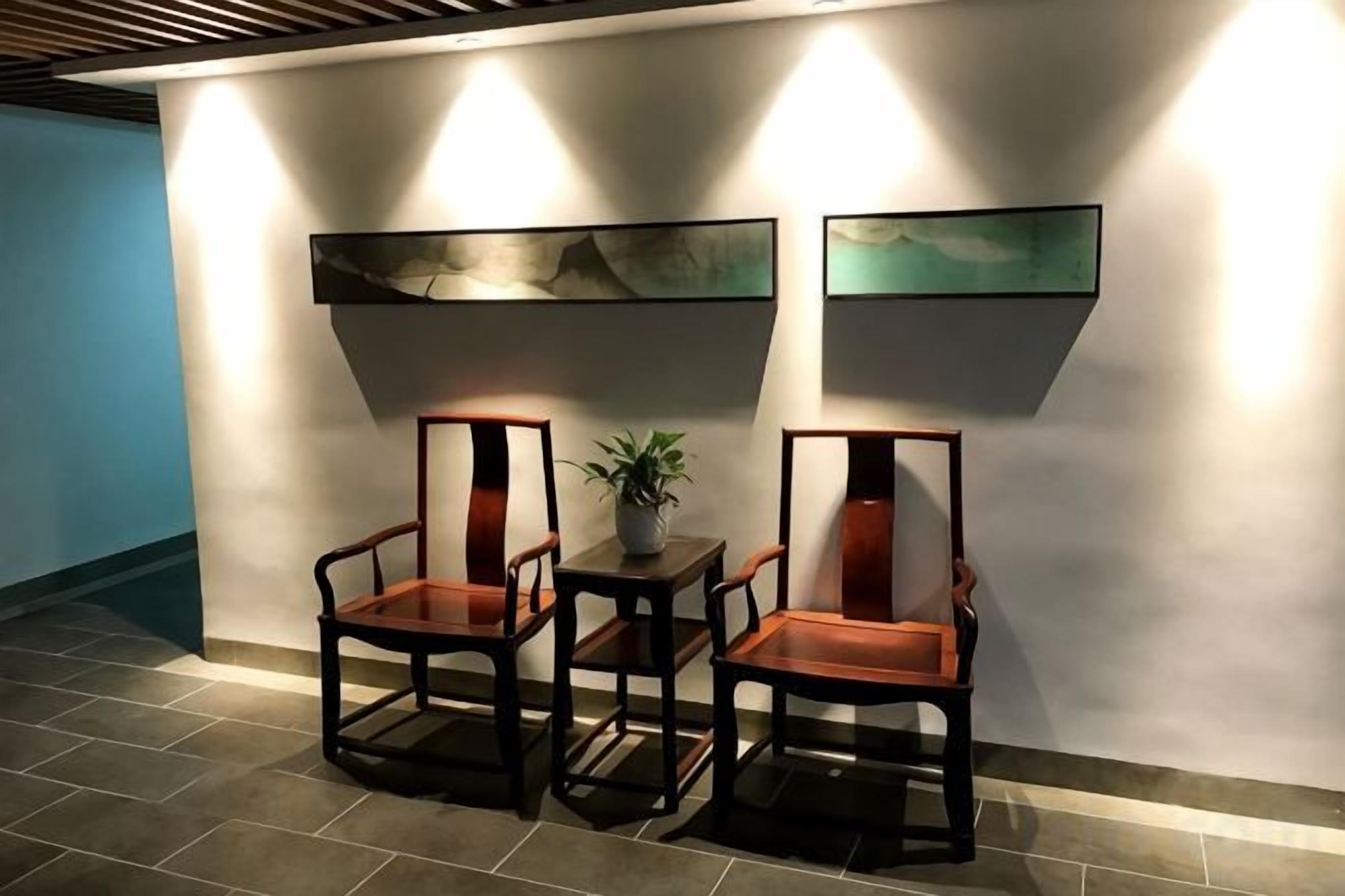 A seating area with two chairs and a small table, a potted plant, and two wall-mounted artworks.