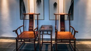 A room with two wooden chairs and a small table, with traditional artwork on the wall.