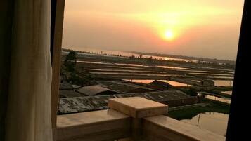 A view of a sunset over a rice paddy field from a balcony with a railing.