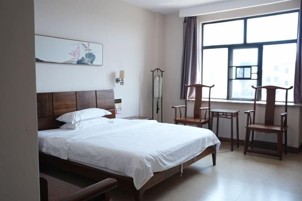 Una habitación de hotel con una cama, dos sillas, una mesa, un ventanal y una obra de arte colgada en la pared.