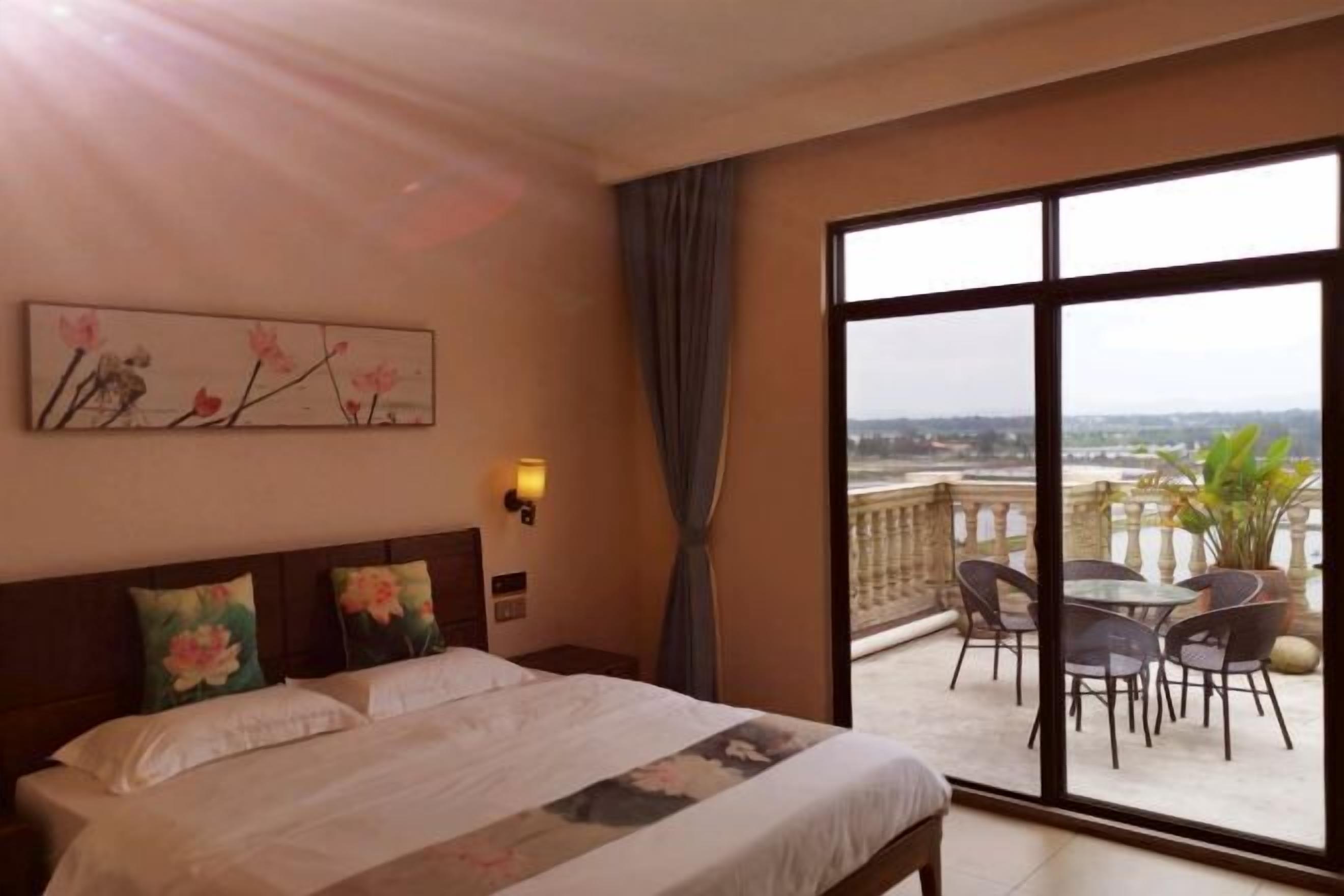 Een hotelkamer met een groot bed, een schilderij aan de muur, een balkon met stoelen en een tafel, en uitzicht op de stad.