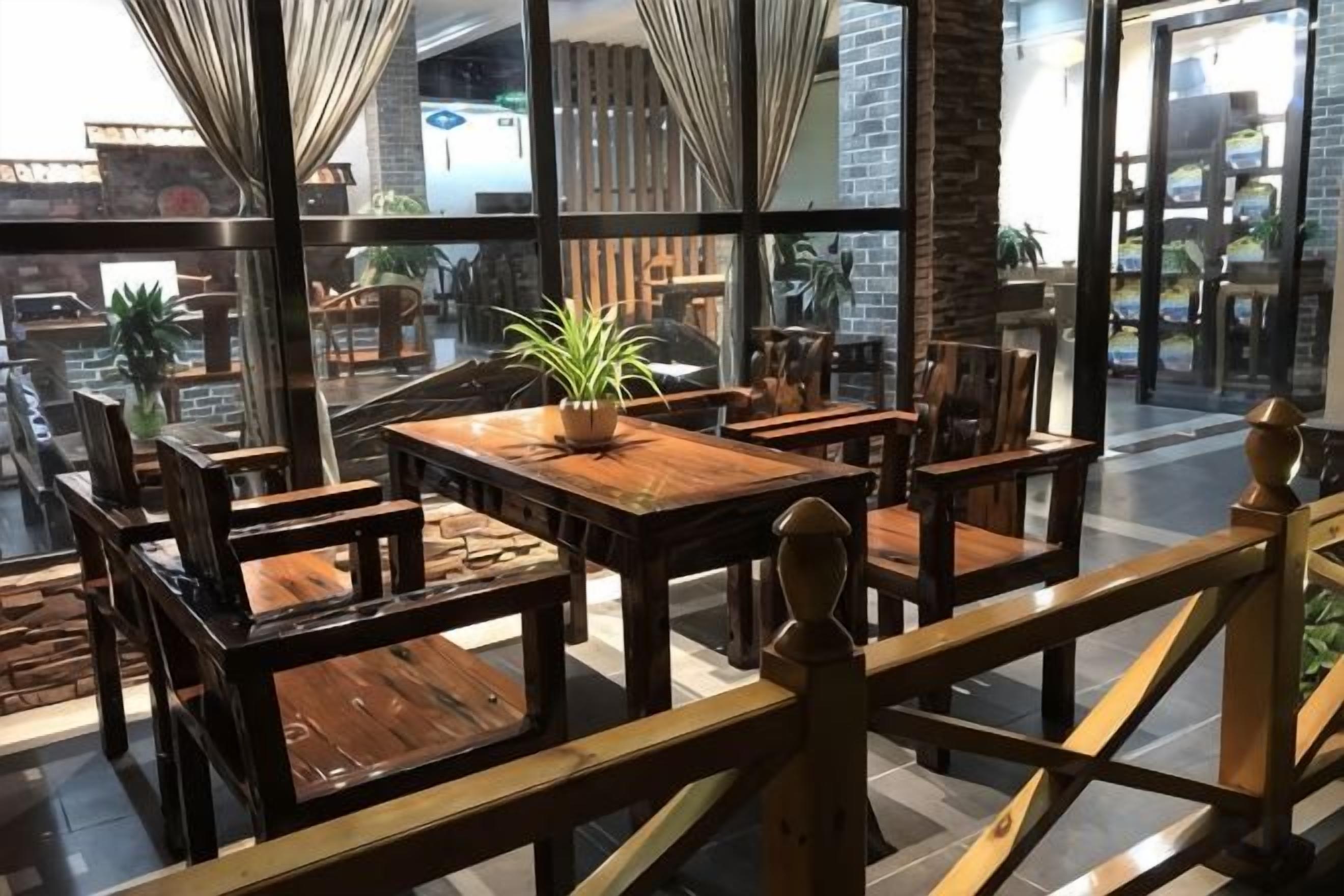 A restaurant with wooden tables and chairs, a potted plant, and large windows offering a view of the street.