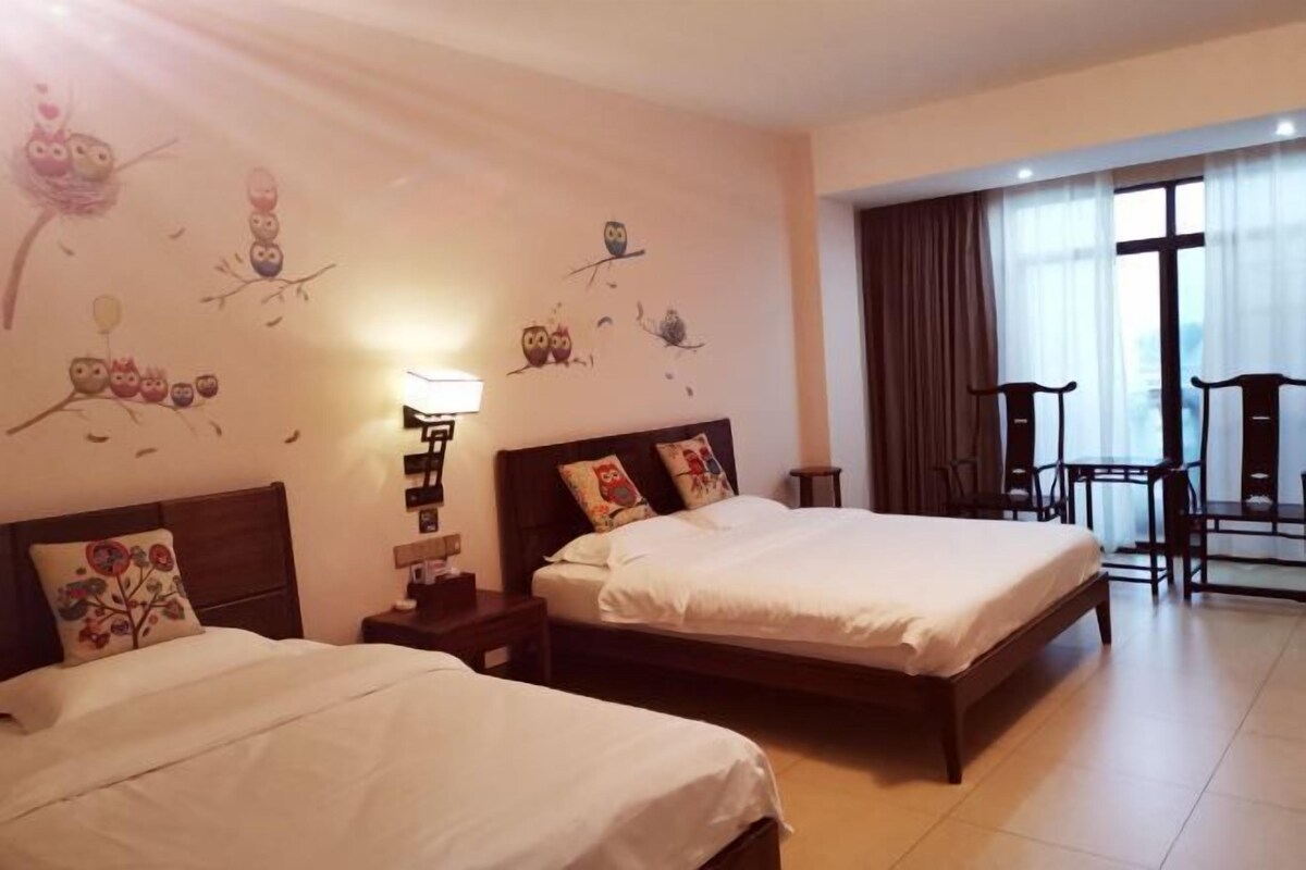 Habitación de hotel con dos camas, una mesita de noche, una lámpara, una ventana con cortinas y un área de descanso con sillas.