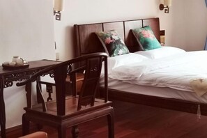 Quarto de hotel com cama de madeira, mesa de cabeceira e uma cadeira.
