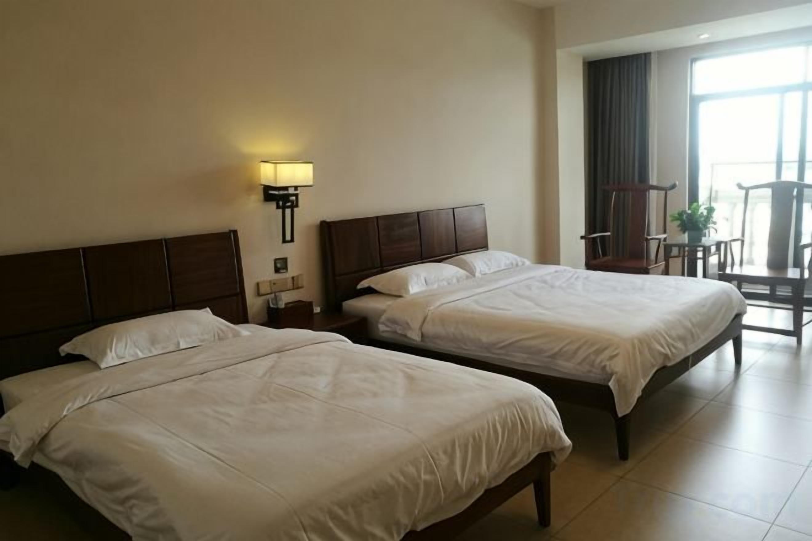 Een hotelkamer met twee bedden, een nachtkastje, een lamp en uitzicht op buiten.