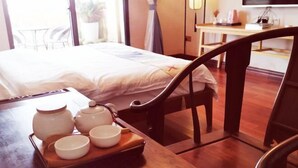 Ein Hotelzimmer mit einem Bett, einem Holztisch mit Teekannen und Tassen sowie Blick ins Freie.