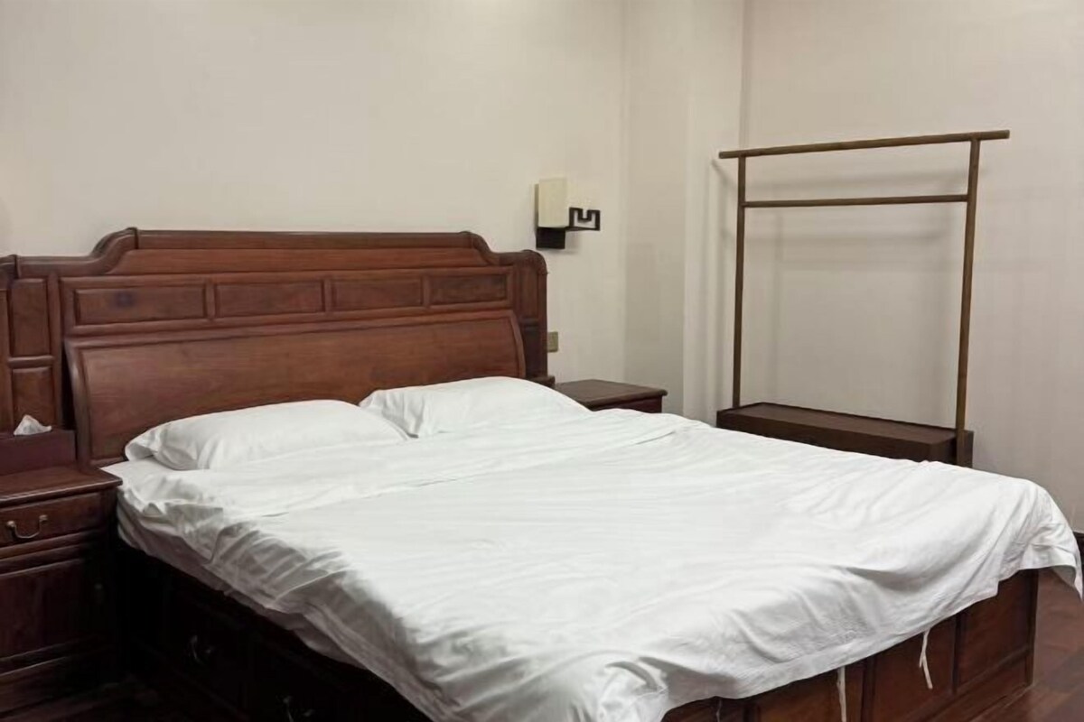 Una cama individual con cabecera de madera, una mesita de noche con lámpara y una estantería en la pared.