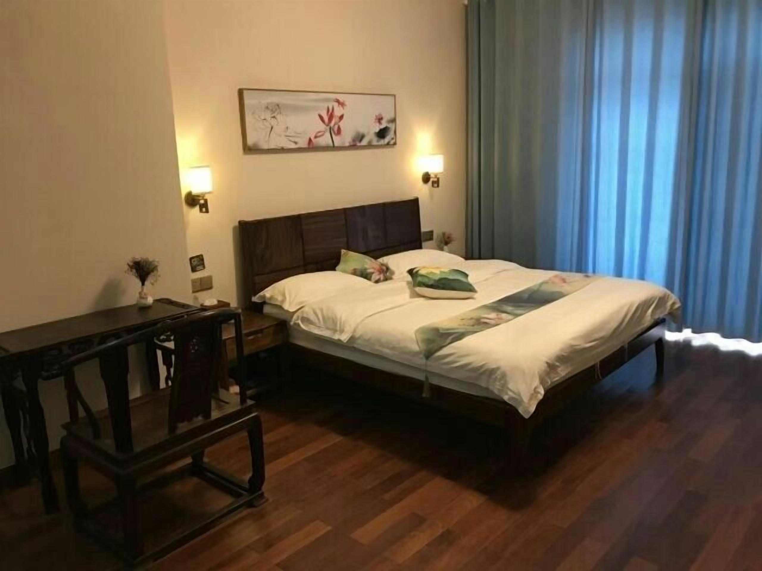 A hotel room with a wooden bed, a nightstand, a desk, and a painting on the wall.