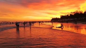 A sunset over a body of water with people walking and standing.