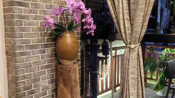 A brick wall, a wooden vase with flowers, and a window with curtains.