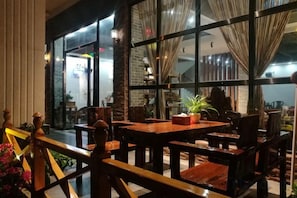 Un comedor interior con mesas y sillas, ventanas amplias y cortinas.
