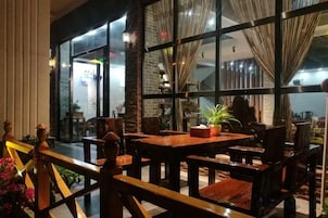 Un comedor interior con mesas y sillas, ventanas amplias y cortinas.