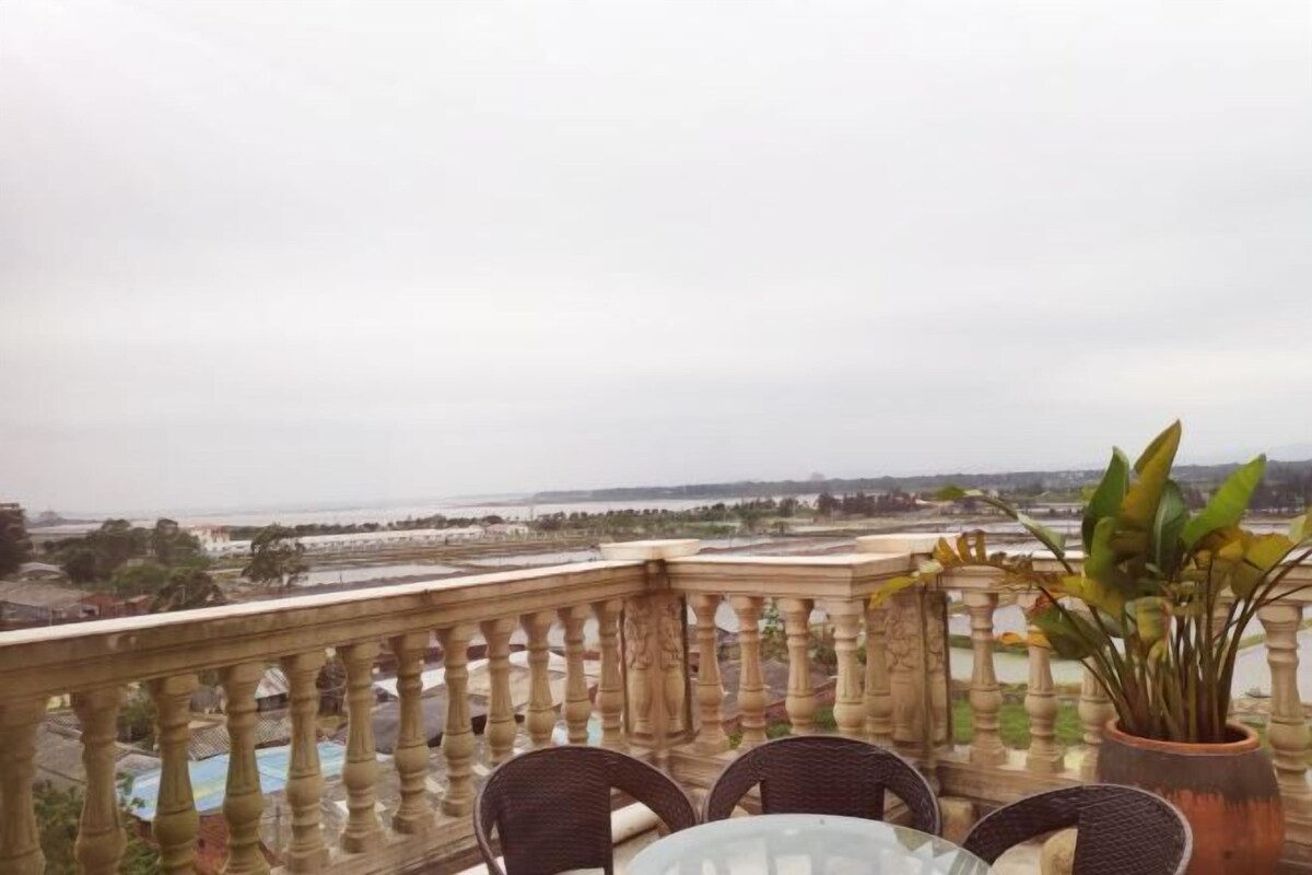 Un balcón con vista al agua, una mesa con sillas y una planta en maceta.