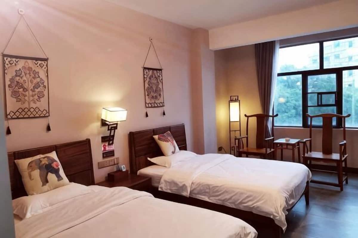 Une chambre d’hôtel avec deux lits, un bureau, des chaises, une lampe et une fenêtre.